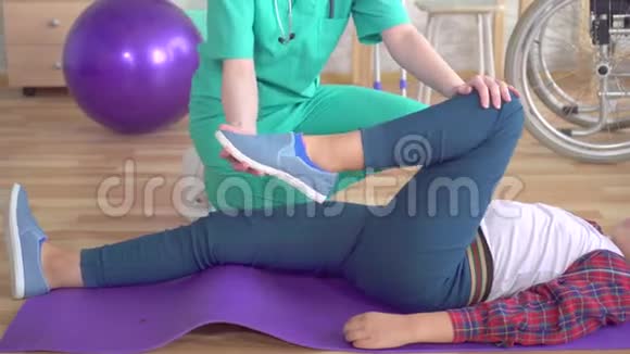 康复中心的物理治疗师帮助一个十几岁的女孩在康复后的腿部做热身运动视频的预览图