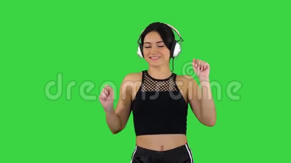 迷人的女孩穿着短裤和耳机在绿色屏幕上跳舞Chroma键视频的预览图
