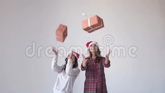 穿着圣诞帽和睡衣的快乐漂亮女孩在白色背景下扔礼物盒等待节日视频的预览图
