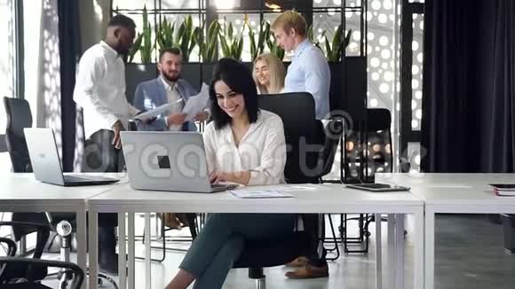 年轻而自信的女商人在办公室里工作时微笑着手提电脑视频的预览图