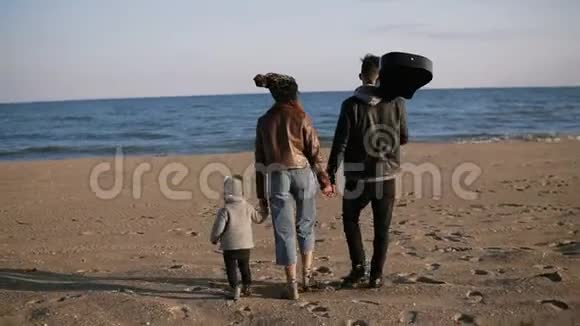 一家人在海滩上散步父母带着他们的小女儿或太阳沿着海滨散步他们手牵手他们是视频的预览图