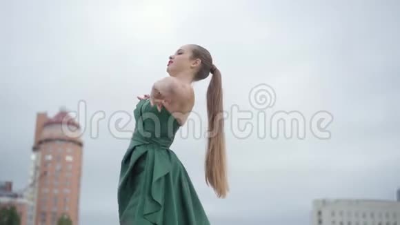 美丽华丽的女孩穿着一件漂亮的晚绿色连衣裙在摩天大楼附近的空城广场上迷人地跳舞视频的预览图