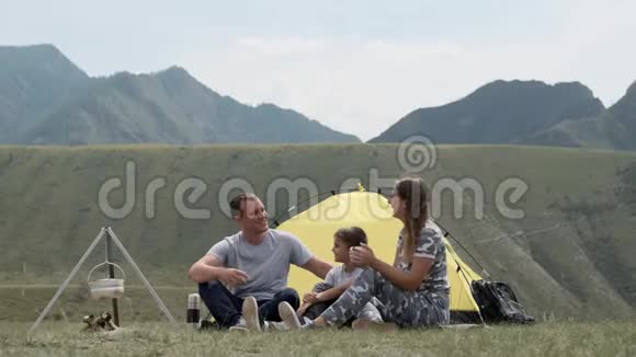 一个幸福的家庭和一个孩子在山上的帐篷前休息喝着热水瓶里的茶视频的预览图