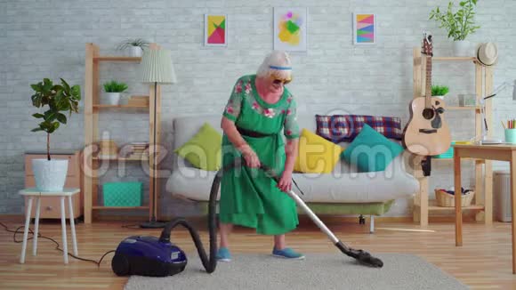 一位快乐的老年妇女戴着灰色头发的老人戴着眼镜像吉他一样吹着吸尘器视频的预览图