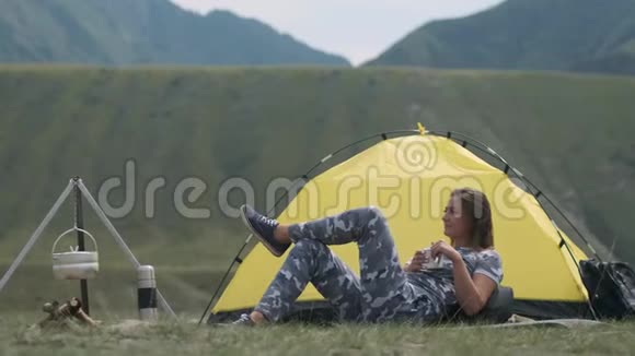 女游客躺在帐篷前在山上放着一杯茶视频的预览图