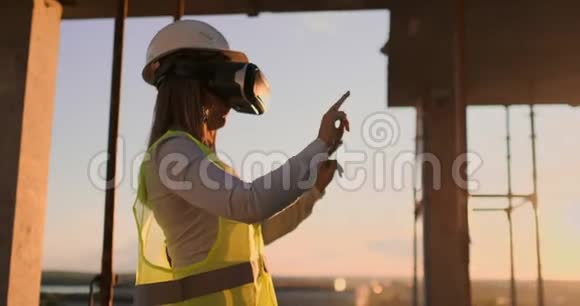日落时分建筑屋顶上的女工程师站在VR眼镜里用手移动视频的预览图