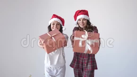 穿着圣诞帽和睡衣的年轻漂亮女人在白色背景上送礼物盒女人手里的小礼物视频的预览图