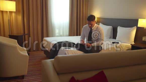 穿着衬衫和领带的人坐在旅馆的床上写在纸上视频的预览图