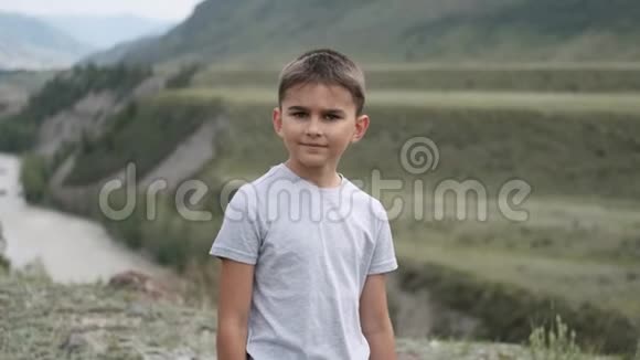 肖像小男孩游客在山和河的背景上看着摄像机视频的预览图