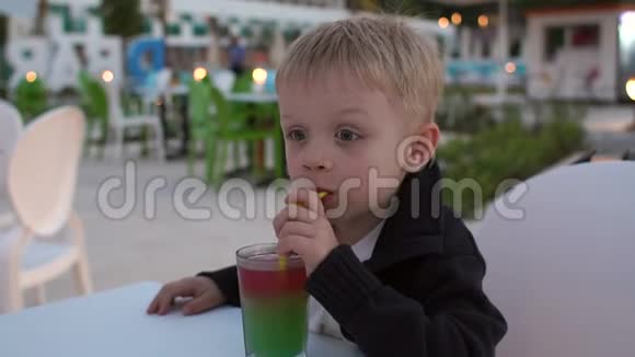 一个小男孩晚上在一家街头咖啡馆里喝着稻草上的果汁视频的预览图