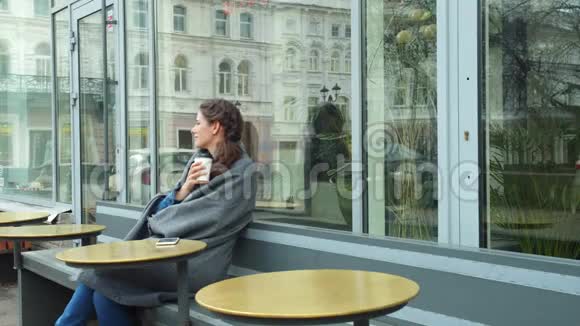 穿着灰毯的女孩坐在外面喝咖啡视频的预览图