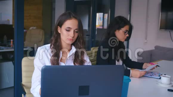 漂亮的年轻女商人在现代办公室里用笔记本电脑工作喝着外卖咖啡视频的预览图