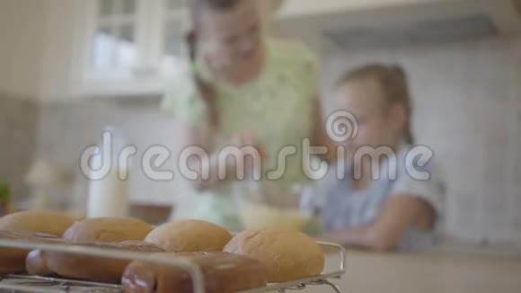 在妈妈和小女儿一起做煎饼或蛋糕的背景下桌子上有新鲜的面包关闭视频的预览图