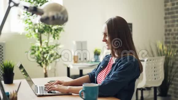在办公室里漂亮女孩带着笔记本电脑微笑着看着屏幕视频的预览图