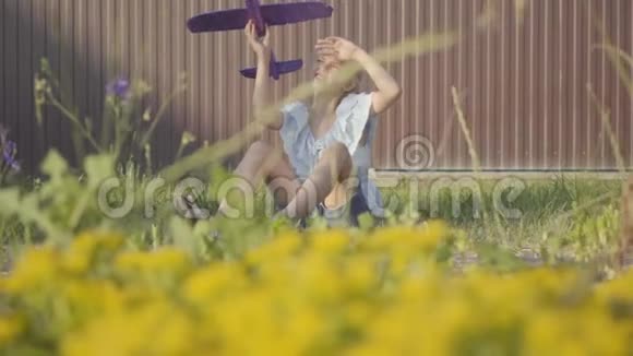 可爱的女孩带着玩具飞机坐在院子里的绿草上在户外玩的女孩无忧无虑的童年慢慢视频的预览图