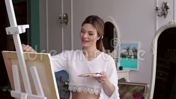 一个穿着白色衬衫的年轻性感女孩在卧室的家中画着帆布艺术视频的预览图