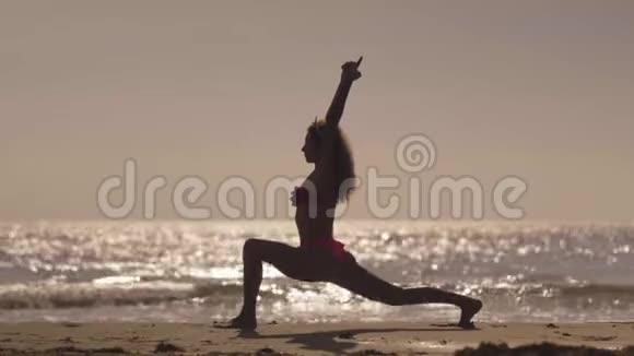 那个女孩日落时在海滩上练习瑜伽在热带海滩做运动的小女孩女性瑜伽剪影视频的预览图