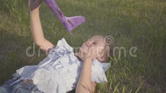 可爱的女孩一架玩具飞机躺在院子里的绿草上在户外玩的女孩视频的预览图