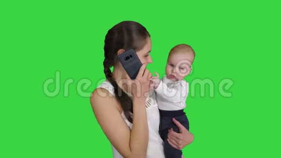 母亲多重任务家庭和人的概念幸福的母亲与婴儿在绿色屏幕上呼唤智能手机视频的预览图