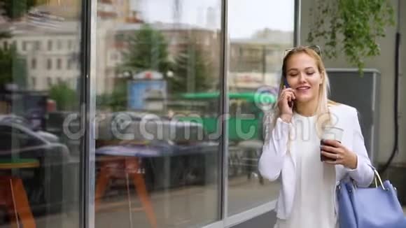 微笑的年轻女子走在街上用手机说话拿着咖啡视频的预览图