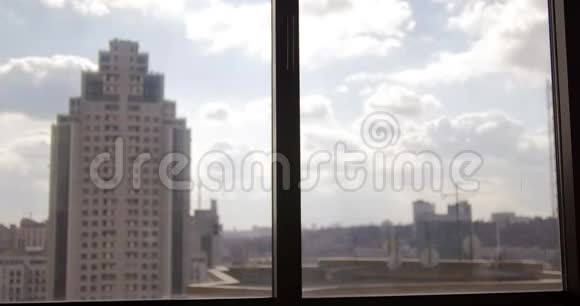 一个穿西装的年轻人走到一个全景窗口欣赏城市的景色窗户城市景观摩天大楼视频的预览图