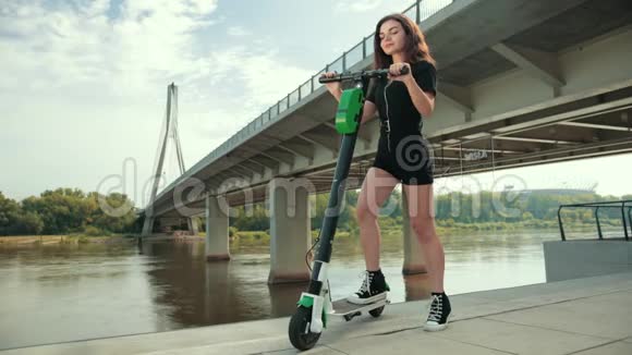 美丽的少女站在河边桥边有电动滑板车视频的预览图