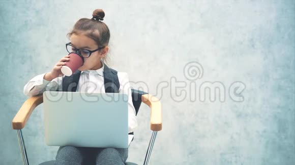 一个小女老板坐在椅子上拿着笔记本电脑灰色背景特写镜头喝茶视频的预览图