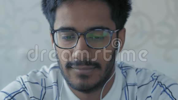 特写镜头戴眼镜和耳机的印度男人看着笔记本电脑上的广播新闻视频的预览图