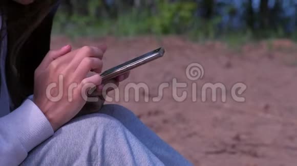 女人正在浏览智能手机坐在自然侧视手特写视频的预览图