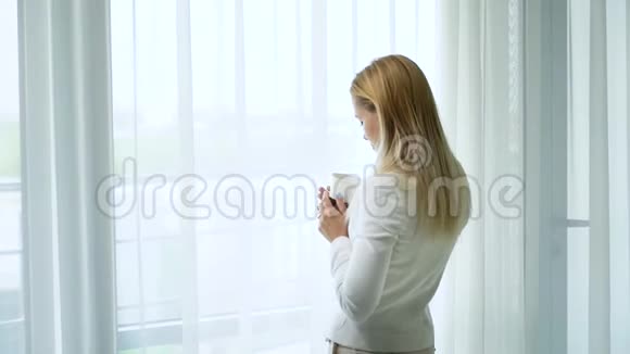 在窗前快乐的年轻已婚女人喝茶做白日梦视频的预览图