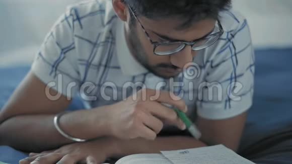 特写镜头戴眼镜的印度学生仔细阅读躺在床上的作品视频的预览图