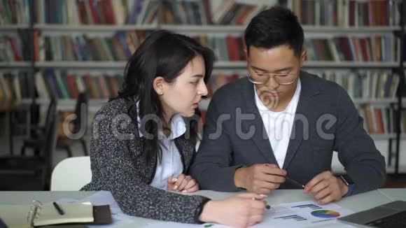 一对亚洲年轻夫妇在图书馆讨论饼图视频的预览图