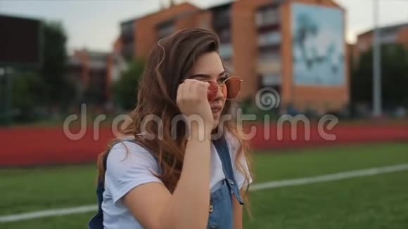 一幅美丽的黑发女人的肖像穿着蓝色的阳光坐在体育场的一个足球球门附近的草坪上阳光照射视频的预览图