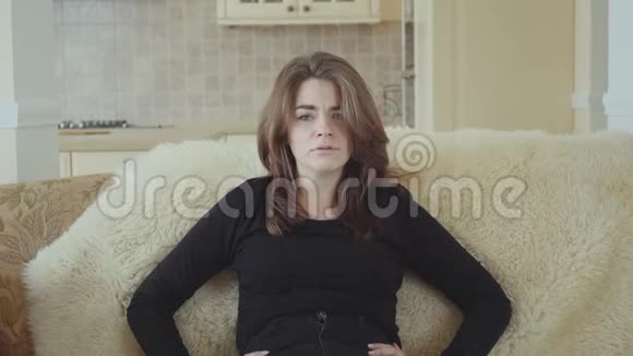 有趣的情绪化的年轻女人坐在沙发上毛茸茸的覆盖物在家里客厅里对着镜头说话视频的预览图