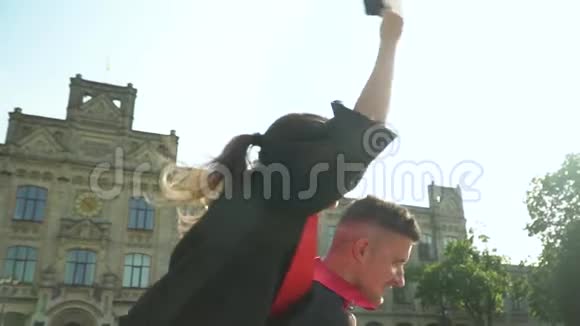 快乐的学生在壁炉前庆祝他们的毕业在大学大楼前坐在上面的女孩视频的预览图