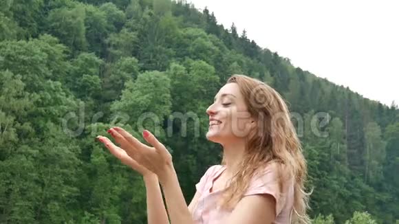 年轻漂亮的金发女郎有着红色的指甲和粉红色的裙子站在寒冷的春雨或秋雨下的山上视频的预览图