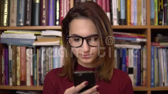 一个年轻的女人正在图书馆看智能手机戴眼镜的女人仔细地看着手机特写在里面视频的预览图