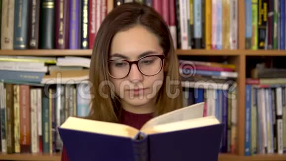 一个年轻的女人正在图书馆看书一个戴眼镜的女人仔细地看着这本书的特写在里面视频的预览图