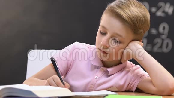 无聊的男孩在课本上写笔记关于功课无趣的主题视频的预览图