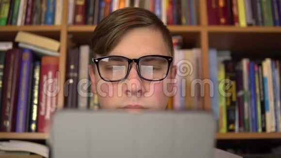 一个年轻人正在平板电脑里读一本书一个戴眼镜的人仔细地看着平板电脑背景是书视频的预览图