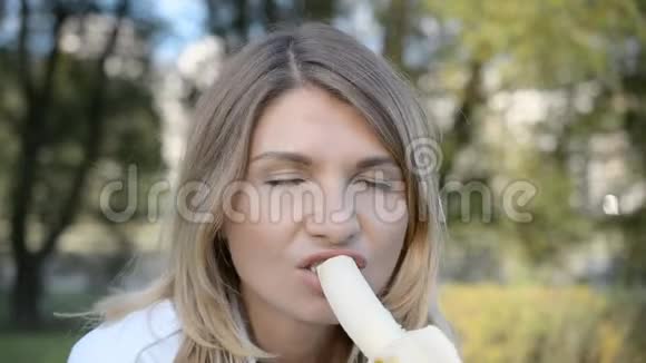 在公园里吃香蕉的金发美女的肖像视频的预览图