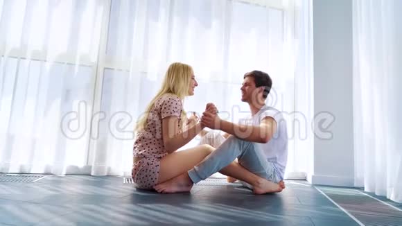 放大年轻夫妇坐在地板上在早晨的阳光下牵手视频的预览图