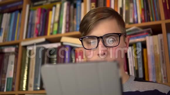 一个年轻人正在平板电脑里读一本书一个戴眼镜的人仔细地看着平板电脑背景是书视频的预览图