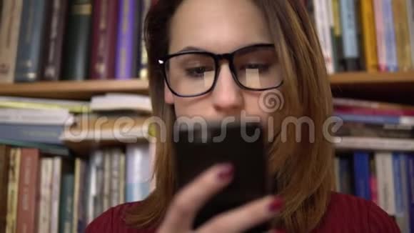 一个年轻的女人正在图书馆看智能手机戴眼镜的女人仔细地看着手机特写在里面视频的预览图