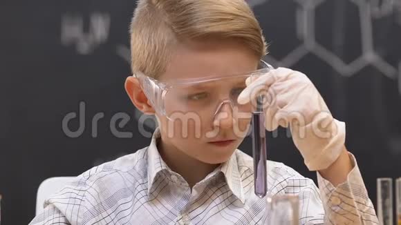 小男孩在化学课上用紫色液体检查试管视频的预览图