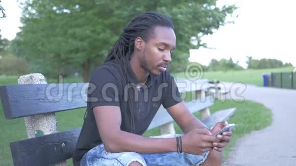 男人坐在公园的长椅上用他的电话视频的预览图