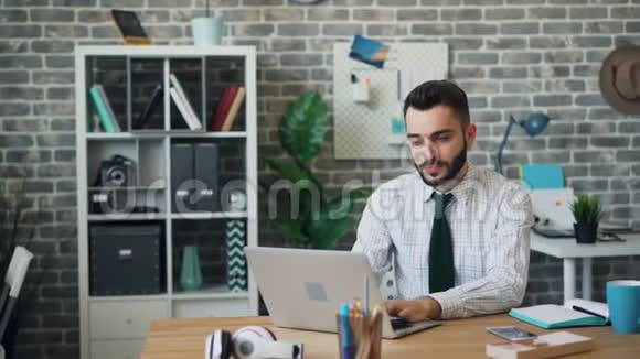年轻男子用笔记本电脑工作然后与同事交谈漂亮的办公室女人视频的预览图