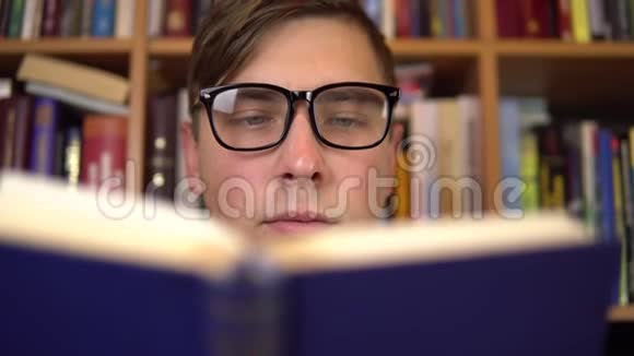 一个年轻人正在图书馆看书一个戴眼镜的人仔细地看了看这本书的特写镜头在后台视频的预览图