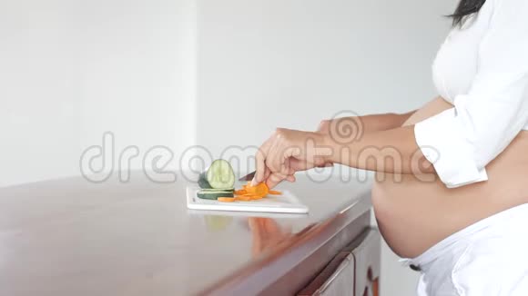 怀孕的拉美妇女站在厨房的木柜台上切菜视频的预览图