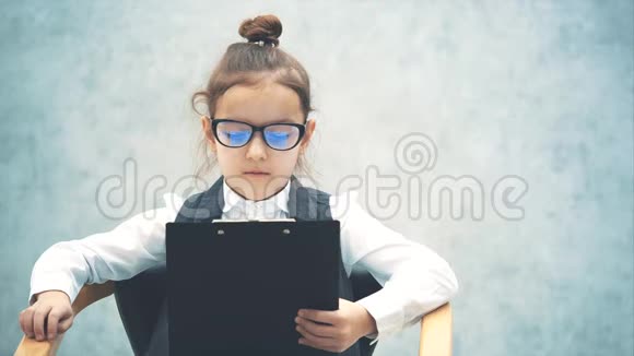 一个小女老板坐在椅子上有一个黑色的文件夹灰色背景戴着眼镜看着一个视频的预览图